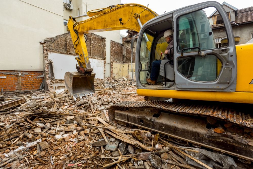 A yellow excavator actively works on a building demolition in Springfield, IL, highlighting local tear down services.